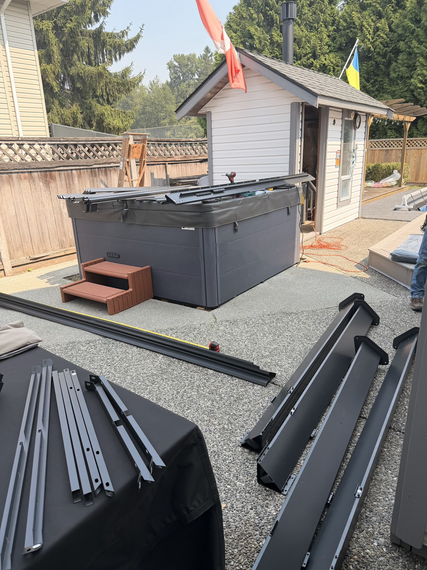 Hot tub sitting uncovered on the patio with the gazebo frame still in pieces on the ground